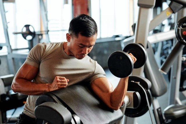 Deportista asiático serio en forma haciendo ejercicio con pesas en el gimnasio